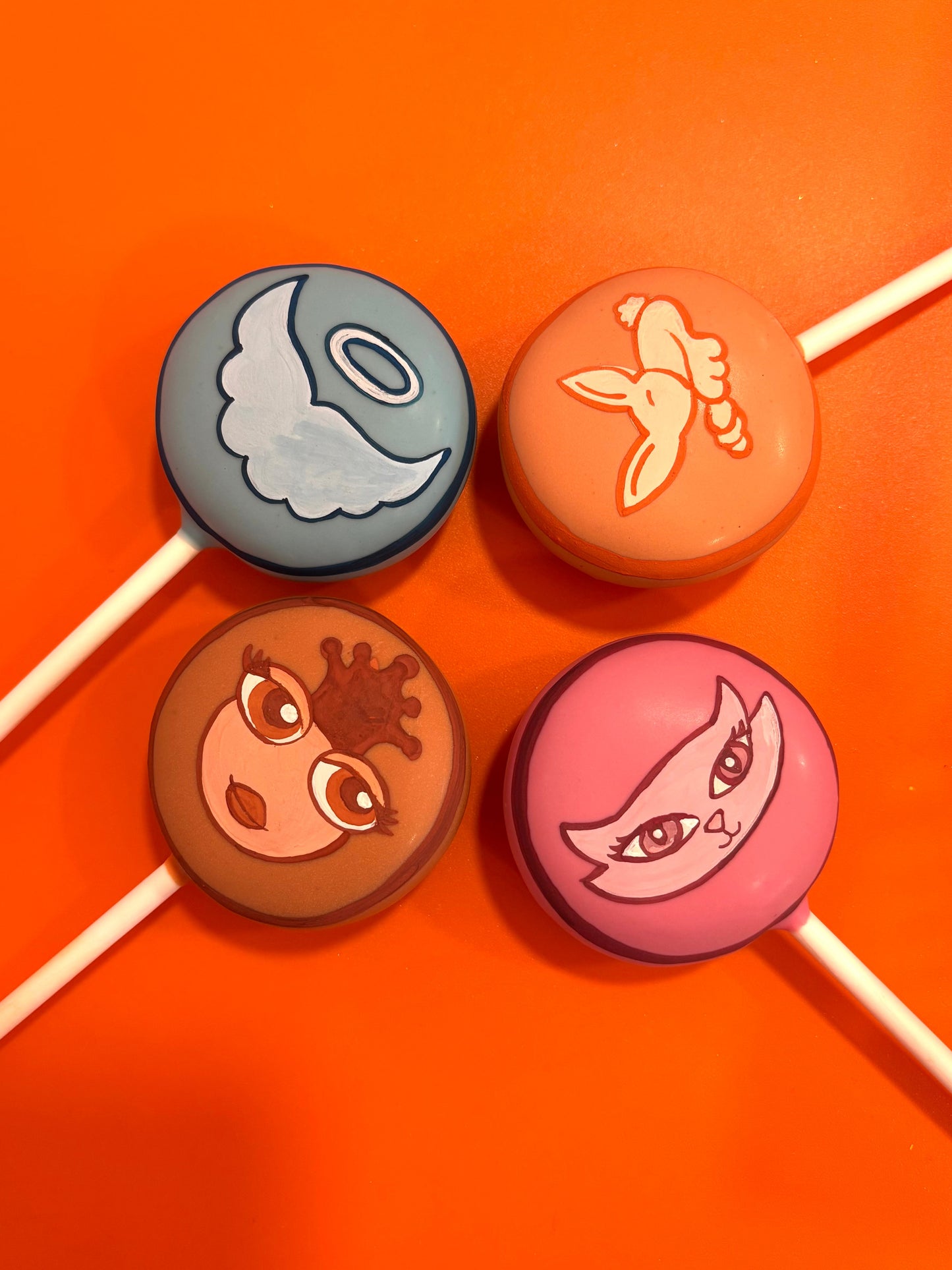 Four cake pops with cartoon character designs on an orange background